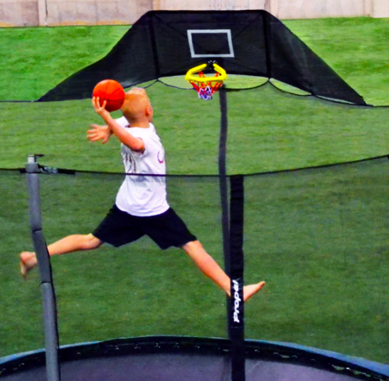 A child dunking a basketball on a trampoline.