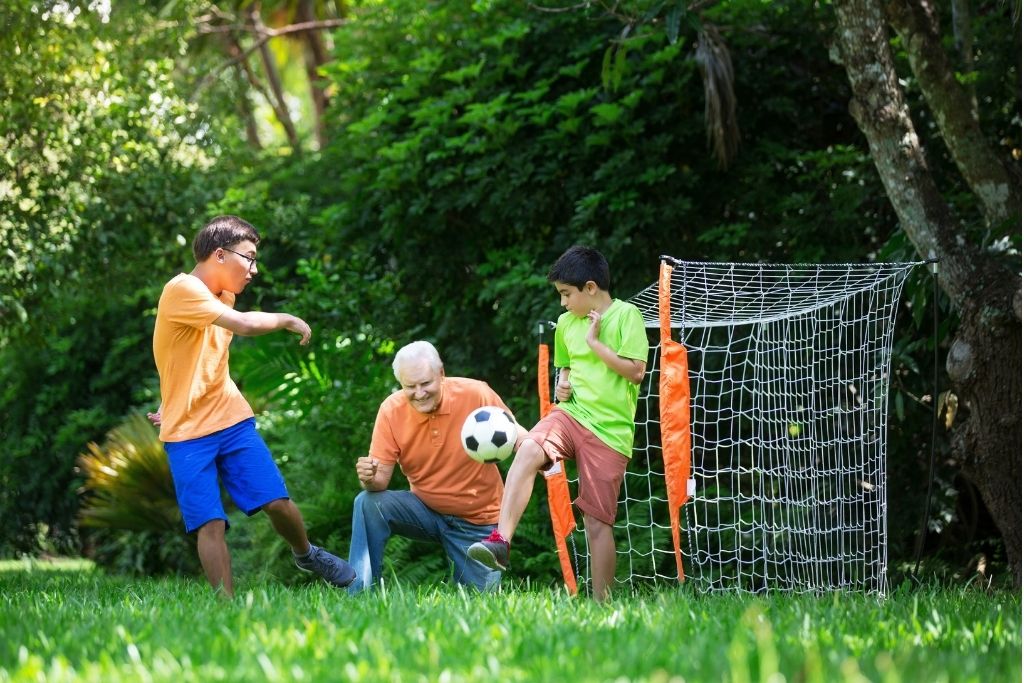 Father and sons play soccer in the backyard.