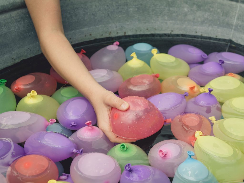 A child grabbing a water balloon from a bucket as she prepares for the balloon toss, one of the most exciting and crazy backyard games for kids.