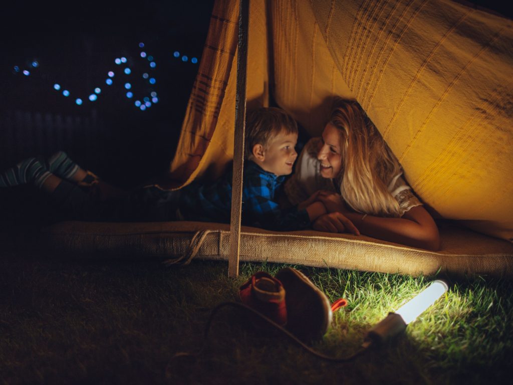 A Mother And Son Camping In Their Backyard With A Flashlight Shining.