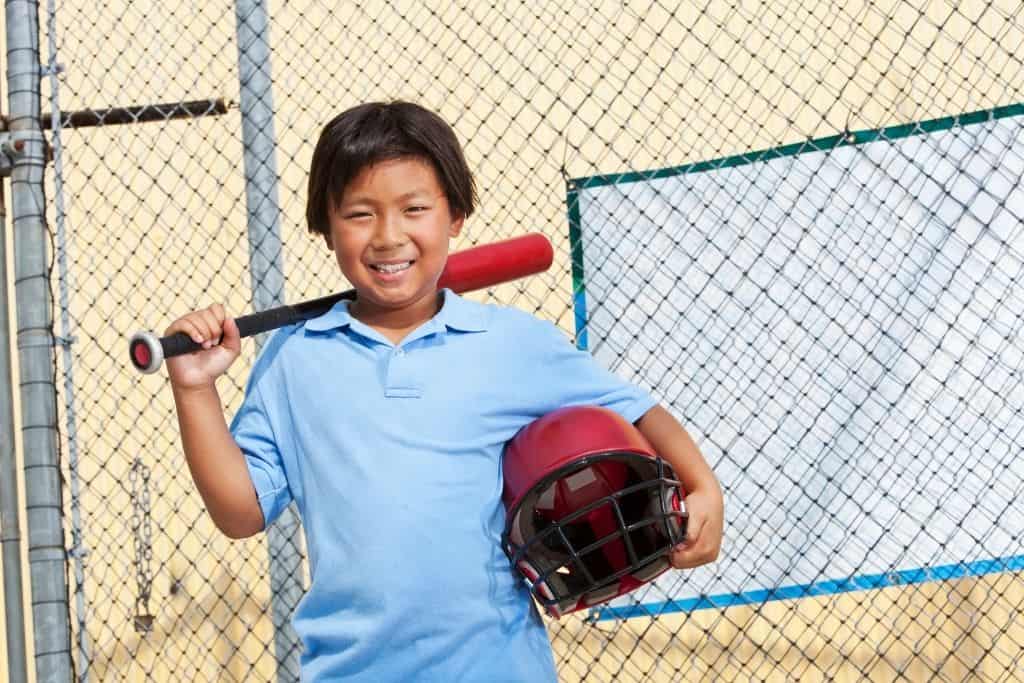 Boy With Baseball Bat and Helmet Playing In A Backyard Batting Cage.