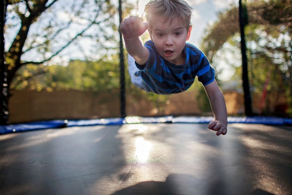 A Little Boy Doing The Superman Pose On A Trampoline.